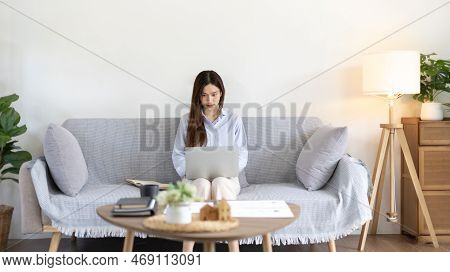 Woman using laptop to work or do homework at home with smiling face in her living room, Creating hap