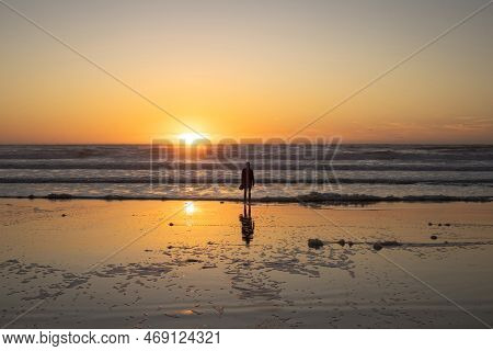 Seascape With Sunset And Silhouette Of A Man Looking Towars The Sun Going Down Across The Ocean