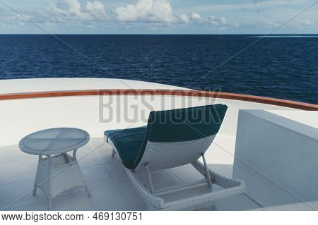 A Wide-angle Shot Of An Outdoor White Recliner (from The Back), With Teal Cushions On It, And A Coff