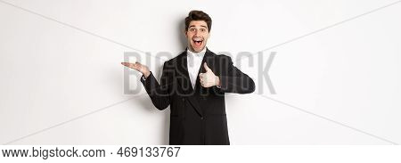 Portrait Of Hadnsome Bearded Man In Formal Suit, Showing Thumb-up And Holding Product In Hand Over W