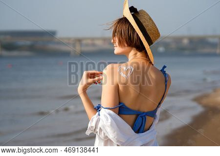 Young Woman In Straw Sunhat And Summersuit With Sun Cream On Tanned Back In Form Heartlet, Shape Hea