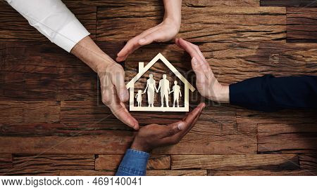 Protecting Family Paper Cut Out With Hands On Wooden Desk
