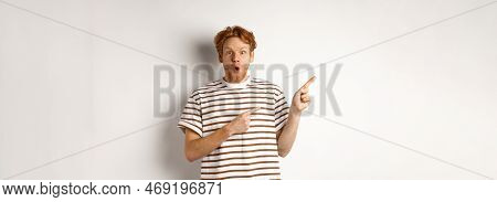 Amazed Man With Ginger Hair Checking Out Promo Offfer, Pointing Left At Logo And Smiling At Camera, 