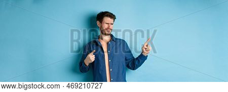 Skeptical Young Man Pointing And Looking Left With Disappointment, Cringe From Something Bad, Standi