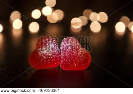 Two Red Sugar Marmalade Candies In Shape Of Heart On Black Background, Lit From Side, Behind Round Y