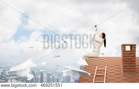 Attractive Young Woman Playing Music On Roof Of Building. Brave Businesswoman With Trumpet Instrumen