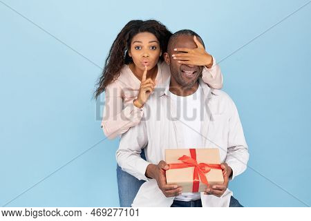 Happy Anniversary. Portrait Of Young Black Woman Covering Her Husbands Eyes, Making Hush Sigh, Givin