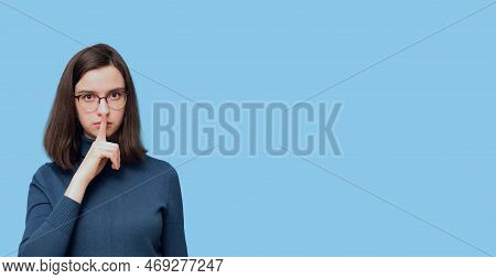 Portrait Of A Serious Student Girl In Glasses And A Sweater Holding A Finger To Her Mouth, A Sign Of