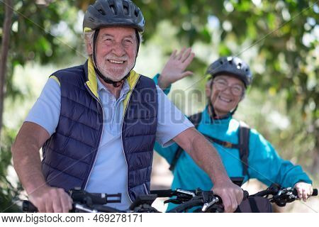 Beautiful Active Senior Couple With Electrobikes Standing Outdoors In The Park. Two Happy Elderly Pe