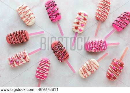 Several Valentine Cakesicles Scattered On A Pink Marble Surface.