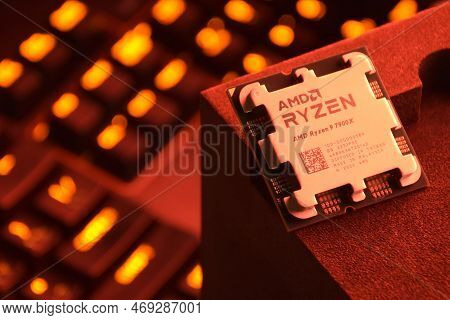 A Close-up Of An Amd Ryzen 9 3900X Processor In A Packaging Box With Backlit Keyboards In The Backgr