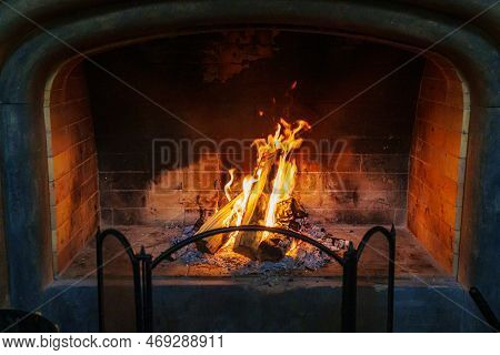 Fireplace With Firewood And A Fire Burning. The Concept Of Home Comfort And Warmth.