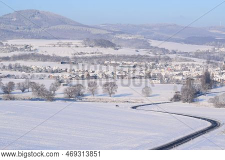 Curvy Road Into Snow Covered Eifel Village Thür With A Volcano Hill In Background