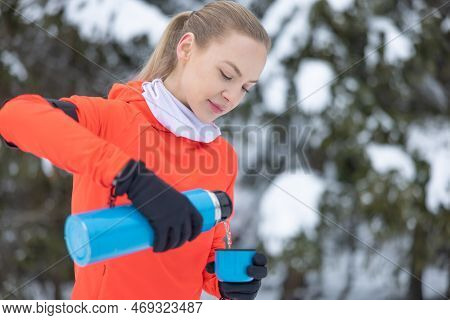 Young Fit Woman In Warm Fitness Clothes Pours Hot Tea Into Mug From Metal Thermos, After Workout Out