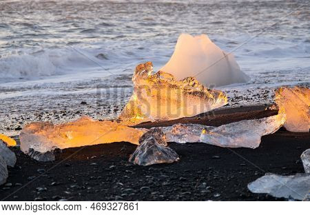Diamond Beach In Iceland. Icebergs Shining On Black Volcanic Sand At Sunset. Clear Ice Crashed By Oc