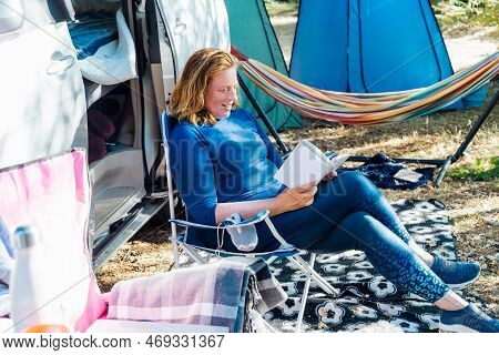 Adult Woman Relaxing, Sitting In The Travel Chair And Reading Book On The Background Of Camper Car V