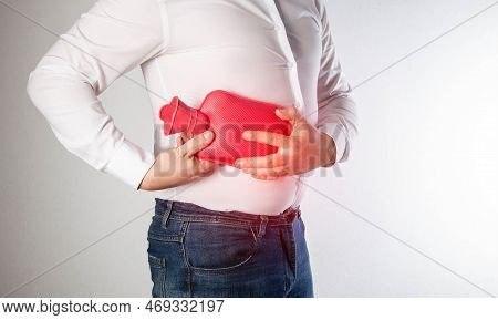 The Man Holds A Heating Pad With Hot Water On The Abdominal Wall On The Right. Relieve Muscle Spasms