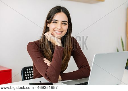 Young Smiling Pretty Adult Woman Sitting At Workplace Looking At Camera. Portrait Of Happy Female St