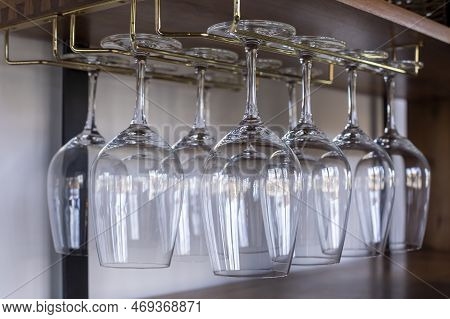 Close Up View Of Clen Clear Wine Glasses Hanging Up Side Down On The Golden Metal Hanger.