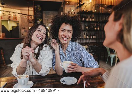 A Group Of Young Women Talking And Laughing Sitting On A Coffee Shop Or Restaurant. Two Ladies Smili