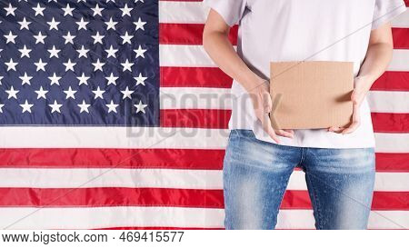 Unrecognizable Woman Is Holding An Empty Cardboard With Space For Text Sign Us Flag On Background. V