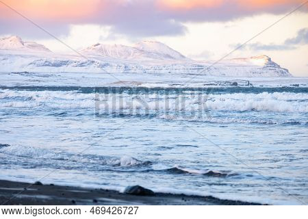 Icelandic Fjords During Sunset. Ocean Coast With Snowy Mountains And Orange Clouds. Winter Landscape