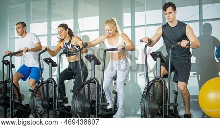 Group Of Young People Doing Exercises On Elliptical Machine At Gym.