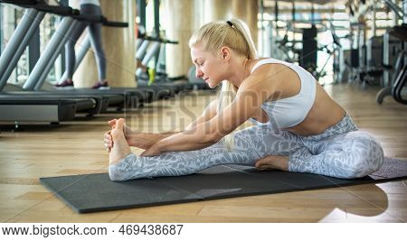 Fitness Blonde Haired Woman Stretching On Exercise Mat At Gym.