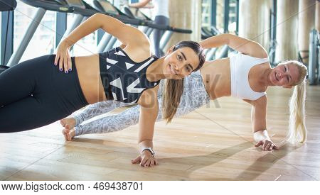 Two Young Women Practicing The Side Plank Pose During Yoga Class In A Gym.