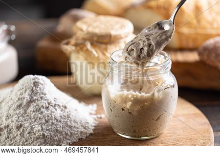 Active Yeast Freshly Ripened On A Spoon, Smooth Flour Next To It And Fresh Bread In The Background.