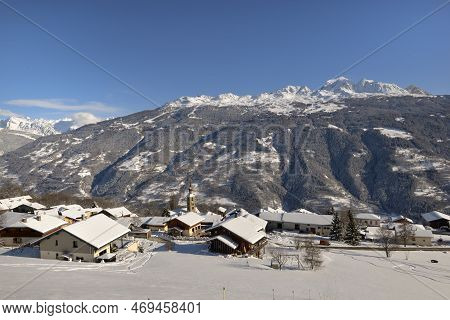 Alpine Village With Snowy Roofs In Tarentaise Valley View On Snowcapped Mountains Under Blue Sky