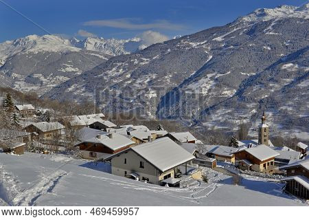 Alpine Village With Snowy Roofs In Tarentaise Valley View On Snowcapped Mountains Under Blue Sky