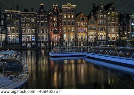 Traditonal Houses And Cruise Boats At The Damrak In Amsterdam In The Netherlands By Night