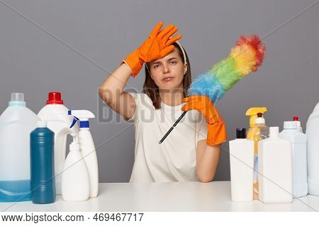 Tired Woman In T-shirt And Orange Gloves, Looks At Camera With Sadness, Sits At Table With Liquid De
