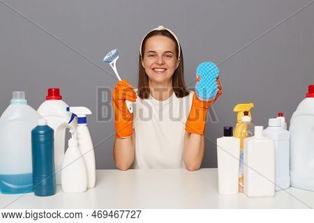 Indoor Shot Of Happy Smiling Woman In White T-shirt And Orange Gloves, Holding Brush And Sponger For