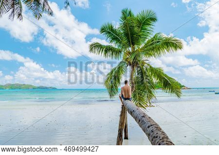 Young Men Sitting At A Palm Tree On A White Tropical Beach Anse Volbert Beach Praslin Seychelles