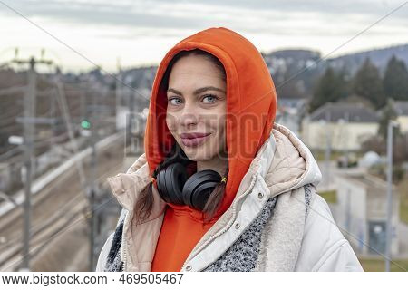 Street Portrait Of A Smiling Young Woman 25-30 Years Old Wearing Headphones On A Neutral Urban Backg