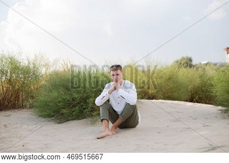 A Man In A White Shirt Sits On The Sand Dunes