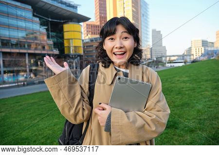 Enthusiastic Brunette Asian Girl, Student With Digital Tablet In Her Hands, Looks Impressed And Surp