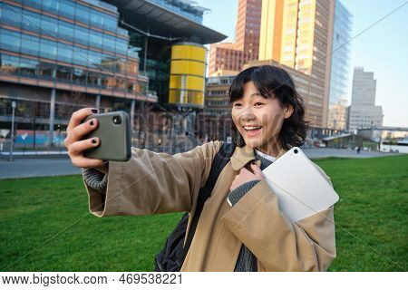 Happy Young Woman, Student Takes Selfie On Street, Holds Her Tablet And Homework Notes, Uses Smartph