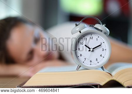 Open Book And Alarm Clock Close Up, Sleeping Woman In Background. Concept Of Overstudy, Overwork And