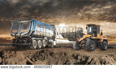 A Loader Or Bedozer Loads A Dump Truck Car With Sand At A Construction Site. Loading A Vehicle For T