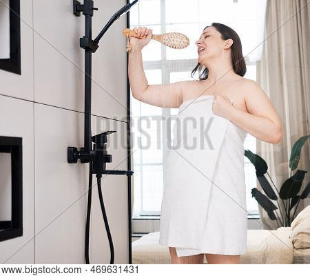 Cheerful Plump Woman In A Bath Towel Pretends To Be A Singer, Standing In The Bathroom Under The Sho