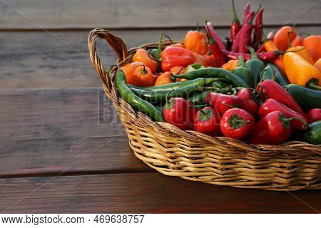Wicker Basket With Many Different Fresh Chilli Peppers On Wooden Table, Space For Text