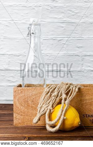 Lemonade Bottle In Crate With Lemon And Grid Bag On Wooden Table. Side View Of Fresh Citrus.