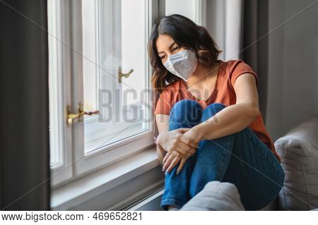 Depressed Young Arab Woman Wearing Protective Mask Sitting Near Windor At Home