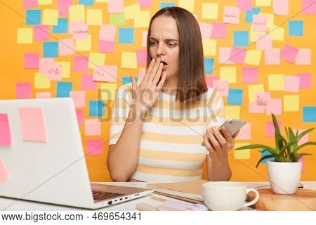 Portrait Of Shocked Scared Woman With Brown Hair Wearing Striped T-shirt Sitting At Table, Looking A