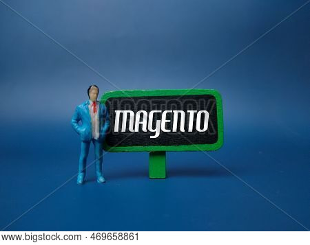 Miniature People And Wooden Board With The Word Magento On Blue Background.