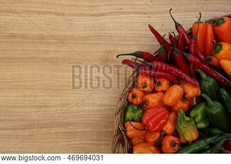 Wicker Basket With Many Different Fresh Chilli Peppers On Wooden Table, Top View. Space For Text
