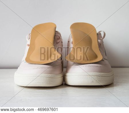 Leather Orthopedic Insoles With Pink Sports Shoes Isolated On White Wooden Board. Foot Care Concepti